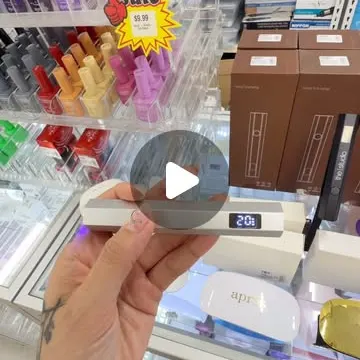 Hand holding a portable LED curing lamp in front of store display shelves.